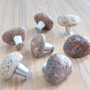 May include: Seven natural stone cabinet knobs with silver metal bases. The knobs are various shades of brown, grey, and red.