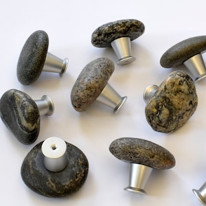 May include: Ten natural stone cabinet knobs with silver metal bases. The knobs are various shades of gray and brown with unique patterns.