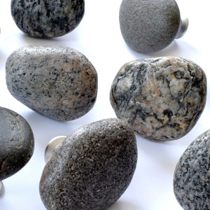 Könnte beinhalten: Ein Satz von neun grauen und braunen Steinknaufknöpfen mit silbernen Metallsockeln. Die Knöpfe sind in verschiedenen Formen und Größen, wobei einige eine texturreichere Oberfläche haben als andere.