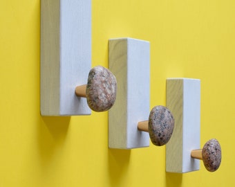 May include: Three white wooden wall hooks with natural stone knobs. The hooks are arranged in a descending size order from left to right.