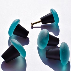 May include: Five teal blue glass cabinet knobs with black metal bases. The knobs have a frosted glass finish.