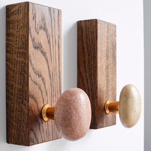 May include: Two wooden wall hooks with stone knobs. The hooks are stained a dark brown and the knobs are a light brown and a reddish brown.
