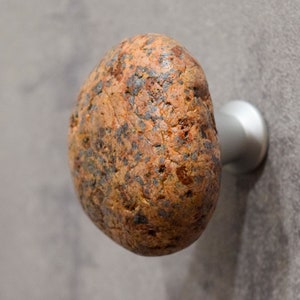 Könnte beinhalten: Ein brauner und orangefarbener Steintürknopf mit einem silbernen Metallsockel.