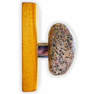 Puede incluir: Un soporte de pared de madera con un pomo redondo de piedra gris moteada. El pomo está unido a la madera con una pieza de metal plateado.