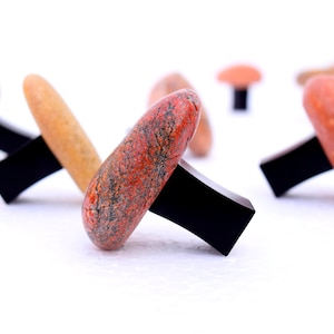 Könnte beinhalten: Eine Gruppe von roten und braunen steinernen, pilzförmigen Schubladenknöpfen mit schwarzen Sockeln.