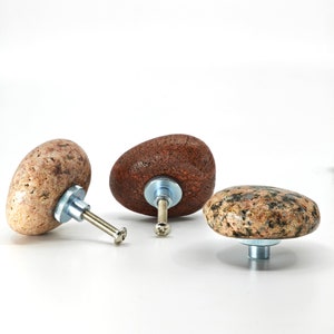 Könnte beinhalten: Drei Steingriffe mit Metallbeschlägen. Die Griffe sind aus verschiedenen Steinsorten gefertigt, darunter braun, beige und rosa mit schwarzen Flecken.