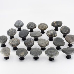 Polished natural stone drawer pulls on a kitchen cabinet, showing unique pebble textures and neutral earthy tones. Handmade beach stone handles bring tactile interest and coastal style to drawers, cupboards, and furniture units, combining functionality with organic design, creating one-of-a-kind decorative accents for modern, rustic, or eclectic home interiors.