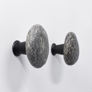 Set of beach stone handles on a light wood wardrobe, showcasing the natural, irregular textures and earthy tones of each stone. Handmade knobs bring subtle tactile appeal to drawers, doors, and storage units, combining organic elegance with functional design, creating a serene and unique coastal-inspired accent for bedrooms, living rooms, or entryways.