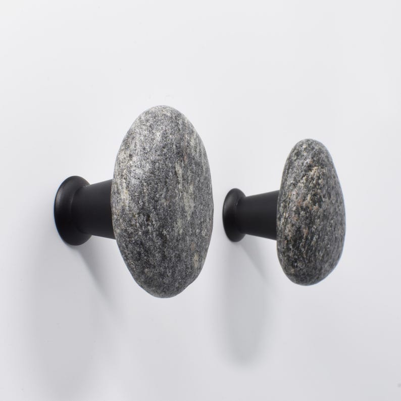 Set of beach stone handles on a light wood wardrobe, showcasing the natural, irregular textures and earthy tones of each stone. Handmade knobs bring subtle tactile appeal to drawers, doors, and storage units, combining organic elegance with functional design, creating a serene and unique coastal-inspired accent for bedrooms, living rooms, or entryways.