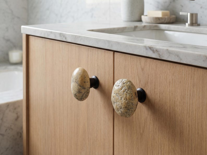 Close-up of unique pebble handles on a chest of drawers, showcasing their polished surfaces and irregular forms. Handmade beach stone drawer pulls add natural charm and tactile interest to nightstands, wardrobes, and storage furniture, combining functional durability with organic design inspired by coastal textures, bringing one-of-a-kind beauty to home interiors.