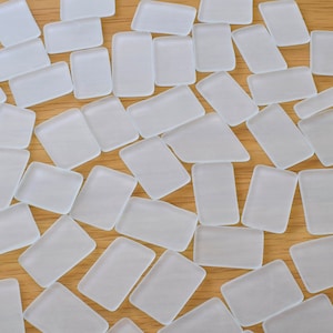 Könnte beinhalten: Eine Sammlung von mattierten Glasfliesen in verschiedenen Größen und Formen, die in einem zufälligen Muster auf einer Holzoberfläche angeordnet sind.