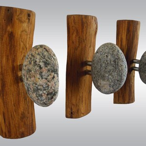 May include: A set of four wooden wall hooks with natural wood grain. Each hook features a rounded, speckled stone attached with metal hardware. The wood has a warm, brown tone, and the stones are gray and beige.