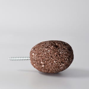 Brown stone round hook shown in a close-up view mounted on a wooden cabinet. The brass threading securely holds the stone in place, making it ideal for use as a functional hook or a decorative knob. This piece combines the beauty of natural stone with durable brass hardware to create a unique, timeless accessory for your home