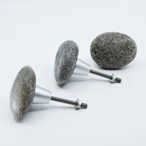 May include: Three grey stone cabinet knobs with silver metal bases and screws. The knobs are shaped like rounded stones.
