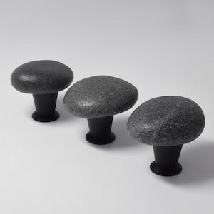 May include: Three mushroom-shaped cabinet knobs. Each knob features a rounded, gray stone top and a black, cylindrical base. The knobs are arranged in a row against a white background, offering a natural, organic aesthetic.