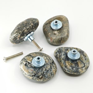 Könnte beinhalten: Vier natürliche Steinknaufgriffe mit silberner Metallbeschläge. Die Knöpfe sind in verschiedenen Grautönen und Braun mit einem gesprenkelten Muster.