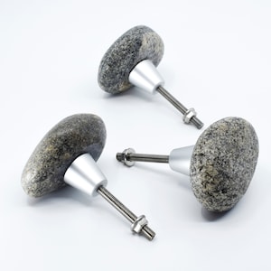 May include: Three stone knobs with silver metal bases and screws. The knobs are gray and have a rough, natural texture.