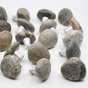 Könnte beinhalten: Eine Sammlung von 15 natürlichen Steinknaufgriffen mit silberner Metallbeschläge. Die Knäufe sind in verschiedenen Grautönen, Braun- und Schwarztönen mit einzigartigen Mustern.