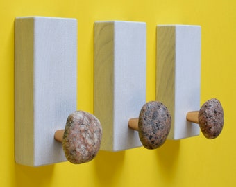 May include: Three white wooden wall hooks with a stone knob on each. The hooks are mounted on a yellow wall.