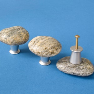 May include: Three stone cabinet knobs with silver bases. The knobs are made of natural stone with a grey and brown colour pattern.