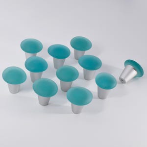 May include: Ten teal blue glass cabinet knobs with silver bases. The knobs are arranged in a semi-circle with one knob off to the side.