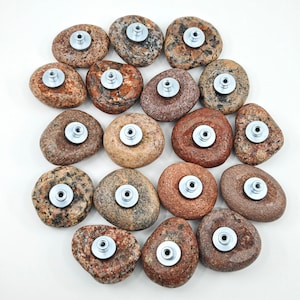 Könnte beinhalten: Eine Sammlung von 16 Untersetzern aus Naturstein mit verschiedenen braunen, grauen und weißen Mustern. Jeder Untersetzer hat einen silbernen Metallknopf in der Mitte.