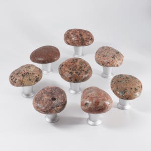 Unique beach stone knobs on a wooden chest of drawers, highlighting smooth, organic pebble forms. These handmade drawer pulls provide functional hardware while adding tactile and visual interest, enhancing coastal, Scandinavian, or farmhouse interiors, and giving furniture a one-of-a-kind handcrafted accent that complements natural and modern home decor.