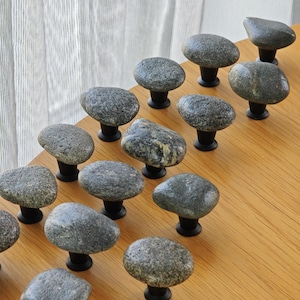 Handmade rock drawer pulls on a minimalist console table, highlighting organic pebble shapes and polished finishes. These natural stone knobs are perfect for drawers, cabinets, or sideboards, providing functional hardware and subtle coastal accents, creating a tactile, visually striking feature that enhances modern, rustic, and eco-conscious interior decor.