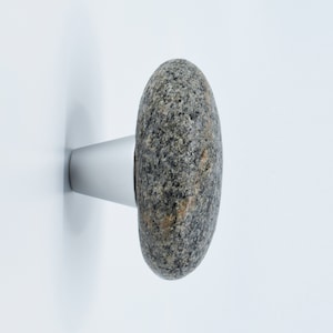 Puede incluir: Un pomo de piedra gris con una base de metal plateado. La piedra es rugosa y texturizada, y la base es lisa y brillante.