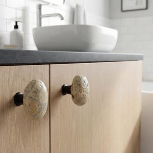 Coastal pebble knobs mounted on a rustic nightstand, emphasizing smooth surfaces and one-of-a-kind natural shapes. Perfect for drawers, bedside tables, or chests, these handmade beach stone handles add tactile charm and understated elegance, enhancing modern farmhouse, Scandinavian, or bohemian interiors with organic, handcrafted accents.