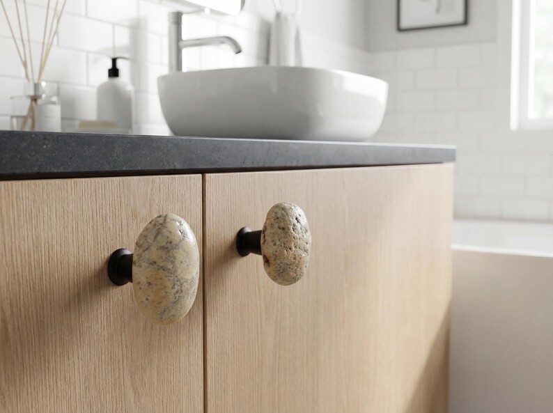 Coastal pebble knobs mounted on a rustic nightstand, emphasizing smooth surfaces and one-of-a-kind natural shapes. Perfect for drawers, bedside tables, or chests, these handmade beach stone handles add tactile charm and understated elegance, enhancing modern farmhouse, Scandinavian, or bohemian interiors with organic, handcrafted accents.