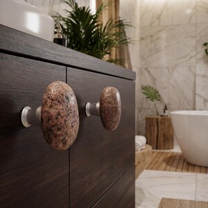 Set of beach stone handles on a light wood wardrobe, showcasing the natural, irregular textures and earthy tones of each stone. Handmade knobs bring subtle tactile appeal to drawers, doors, and storage units, combining organic elegance with functional design, creating a serene and unique coastal-inspired accent for bedrooms, living rooms, or entryways.