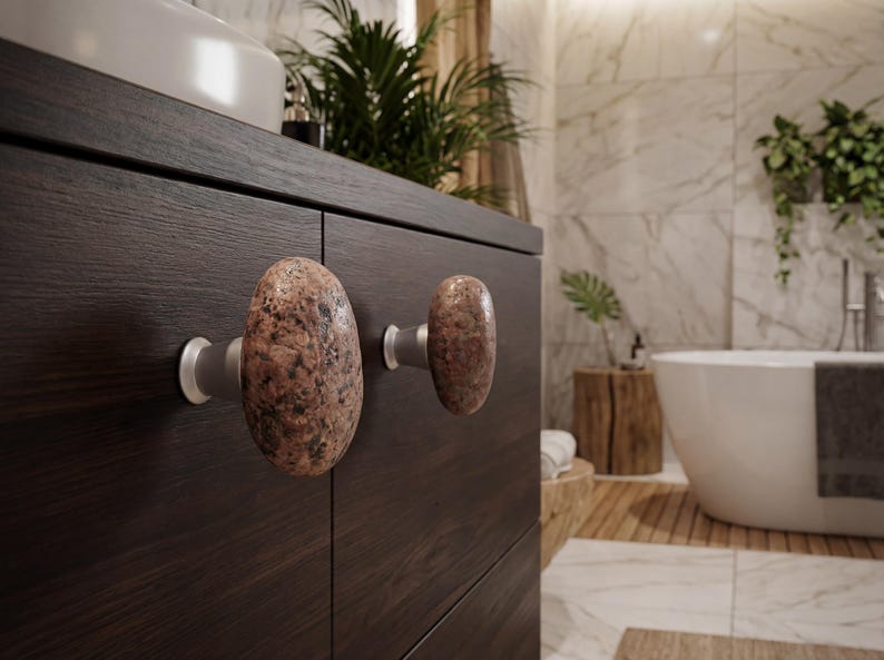 Set of beach stone handles on a light wood wardrobe, showcasing the natural, irregular textures and earthy tones of each stone. Handmade knobs bring subtle tactile appeal to drawers, doors, and storage units, combining organic elegance with functional design, creating a serene and unique coastal-inspired accent for bedrooms, living rooms, or entryways.