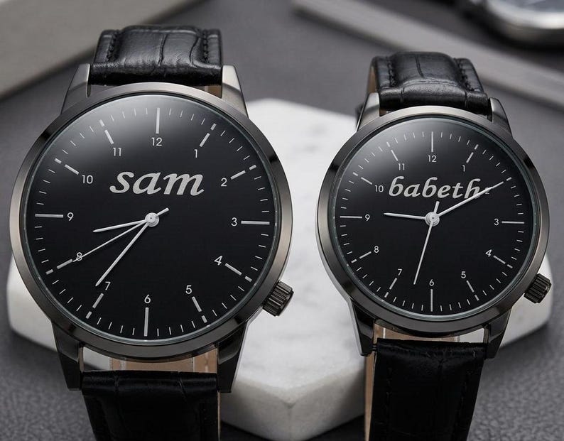 May include: Two black wristwatches with leather straps. One watch face displays the name "sam" in white, the other displays "babeth". Both watches have white hands and hour markers, with a black bezel and case.