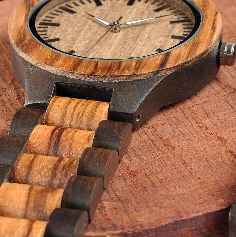 May include: Close-up of a wooden wristwatch with a light brown face and a dark brown wooden band. The watch has silver hands and a silver bezel. The band is made of alternating light and dark brown wooden links.
