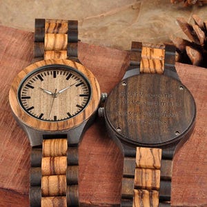 May include: Two wooden watches with a light brown face and dark brown wooden band. The watch face has black hour markers and silver hands. The back of one watch is engraved with the words "Every second, I love you more. Love, Michael 06.06.2018."