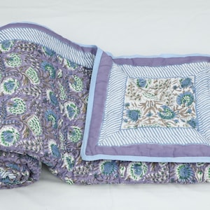 May include: A rolled-up, floral-patterned quilt in shades of purple, blue, and green. The quilt features a repeating floral design and a striped border. The quilt is made of soft fabric and is suitable for a bed or sofa.