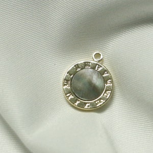 Puede incluir: Un colgante dorado con una incrustación redonda de nácar con marcas de números romanos.