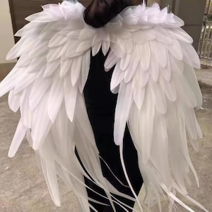 May include: Large white feathered wings featuring layered, pointed plumage that extends outward from a central point. The wings are constructed with numerous individual white feathers arranged in a dense, overlapping pattern to create a full, expansive shape.