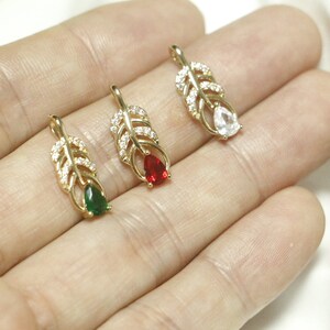May include: Three gold feather pendants with clear, red, and green gemstones. Each pendant features a detailed feather design with small clear stones.