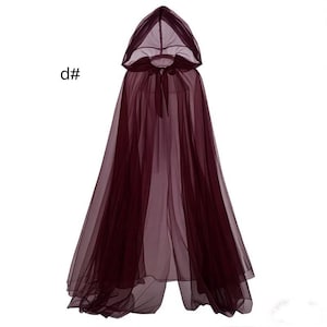 Puede incluir: Una capa con capucha de color burdeos oscuro que llega hasta el suelo, hecha de tela de tul transparente superpuesta. La prenda cuenta con una capucha puntiaguda y un cierre de lazo de tela a juego en el cuello. El texto "d#" es visible a la izquierda.