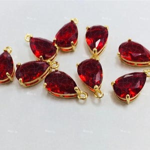 May include: Eight red teardrop-shaped glass charms with gold-tone metal settings and loops. The charms are perfect for jewelry making or adding a touch of sparkle to crafts.