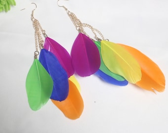 Könnte beinhalten: Ein Paar lange, bunte Federohrringe. Jeder Ohrring besteht aus einer Kette mit mehreren Federn in den Farben Grün, Blau, Lila, Gelb und Orange.