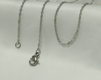 May include: A silver chain necklace with a lobster clasp closure. The chain is made of small, linked circles.