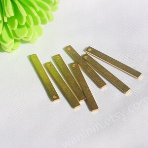 May include: Eight gold-colored metal bar pendants with a hole at each end. The bars are arranged in a fan shape on a white surface.