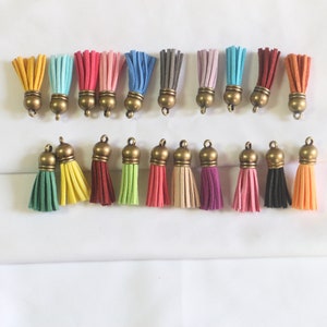 Könnte beinhalten: Sortiment von 20 bunten Quastenanhängern mit goldfarbenen Metallkappen. Die Quasten sind aus weichem Wildleder gefertigt und in verschiedenen Farben erhältlich, darunter Rot, Blau, Grün, Gelb, Rosa und Braun.