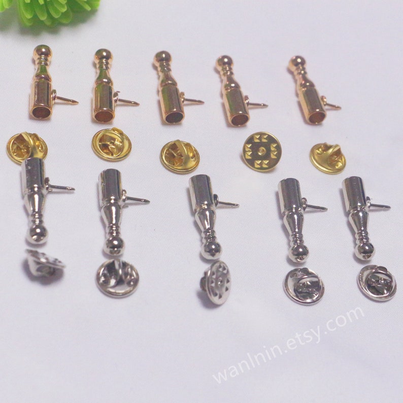 K&ouml;nnte beinhalten: Ein Set mit 10 goldenen und silbernen Metall-Stiftverschl&uuml;ssen f&uuml;r Bastelarbeiten und Schmuckherstellung. Die Stiftverschl&uuml;sse sind flaschenf&ouml;rmig und haben eine runde Oberseite. Die Stiftverschl&uuml;sse sind in zwei Gruppen unterteilt, eine Gruppe in Gold und eine Gruppe in Silber.