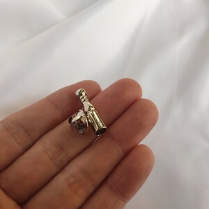 K&ouml;nnte beinhalten: Ein silberfarbener Flaschenverschluss mit einem korkf&ouml;rmigen Oberteil und einem flaschenf&ouml;rmigen Unterteil. Der Verschluss wird in einer Hand gehalten.