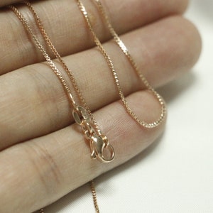 May include: A delicate gold chain necklace with a lobster clasp closure. The chain is made of a fine, box-style link.