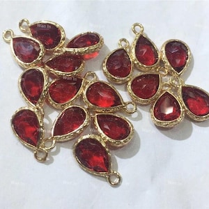 May include: A group of 15 red teardrop-shaped glass charms with gold-tone metal settings. The charms have a textured surface and are ideal for jewellery making.